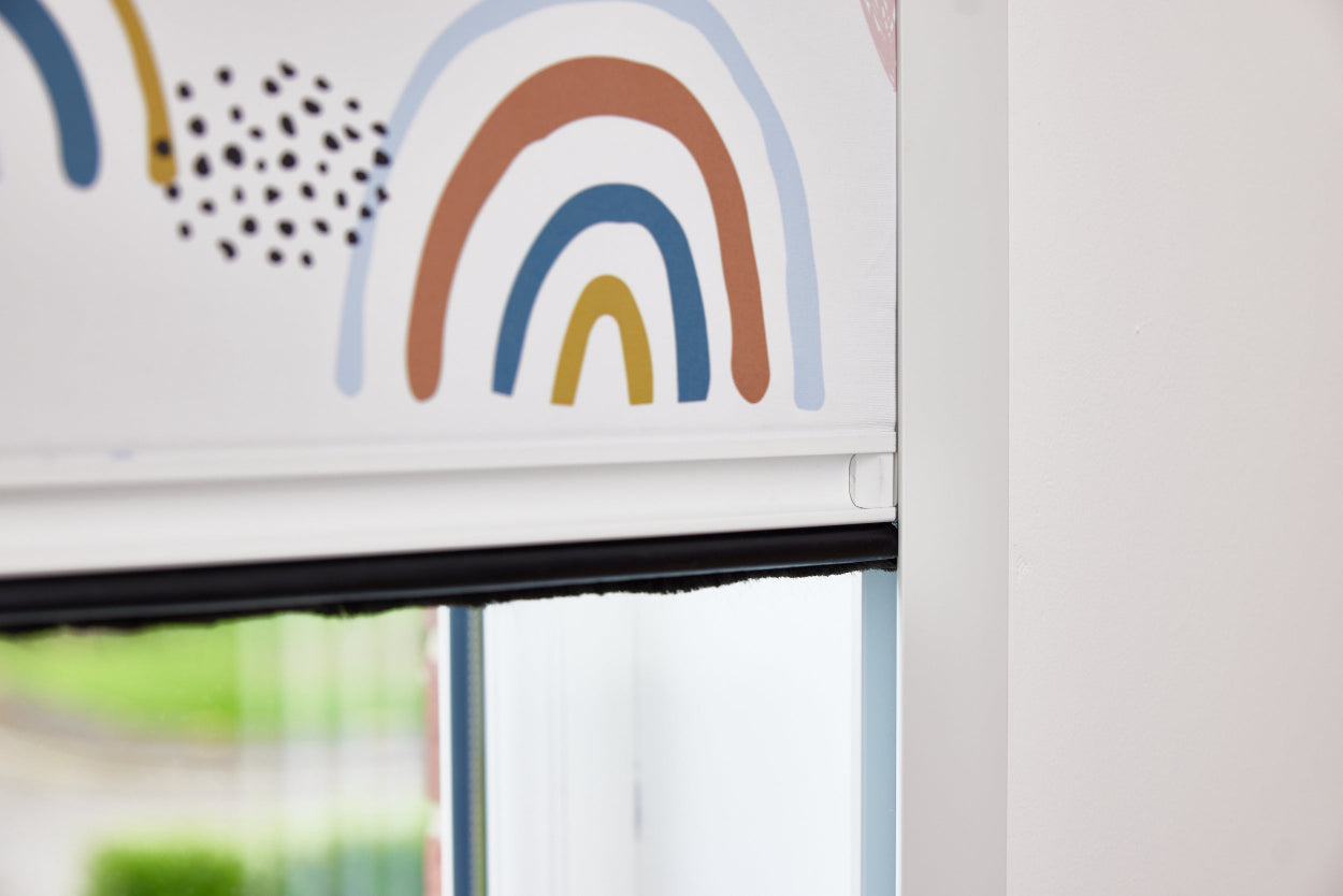 A close-up photo of a BlocOout blind with a children's rainbow on the fabric.