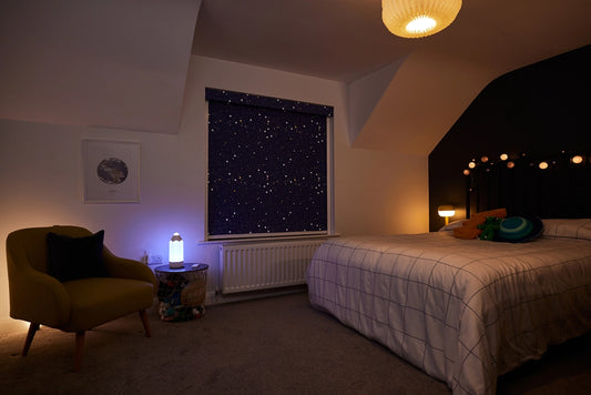 A warmly lit children's bedroom with a BlocOut blind that features a night sky fabric.
