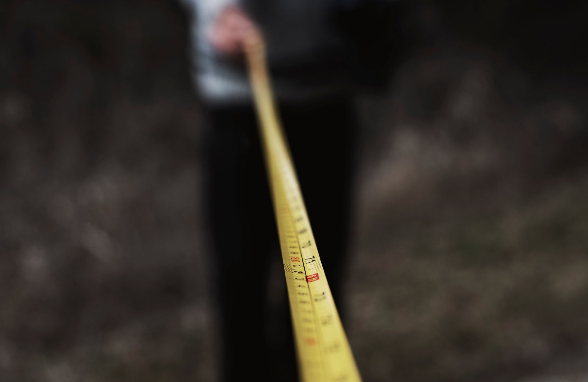 A close up of a tape measure. I person in the background is holding one end of the tape.