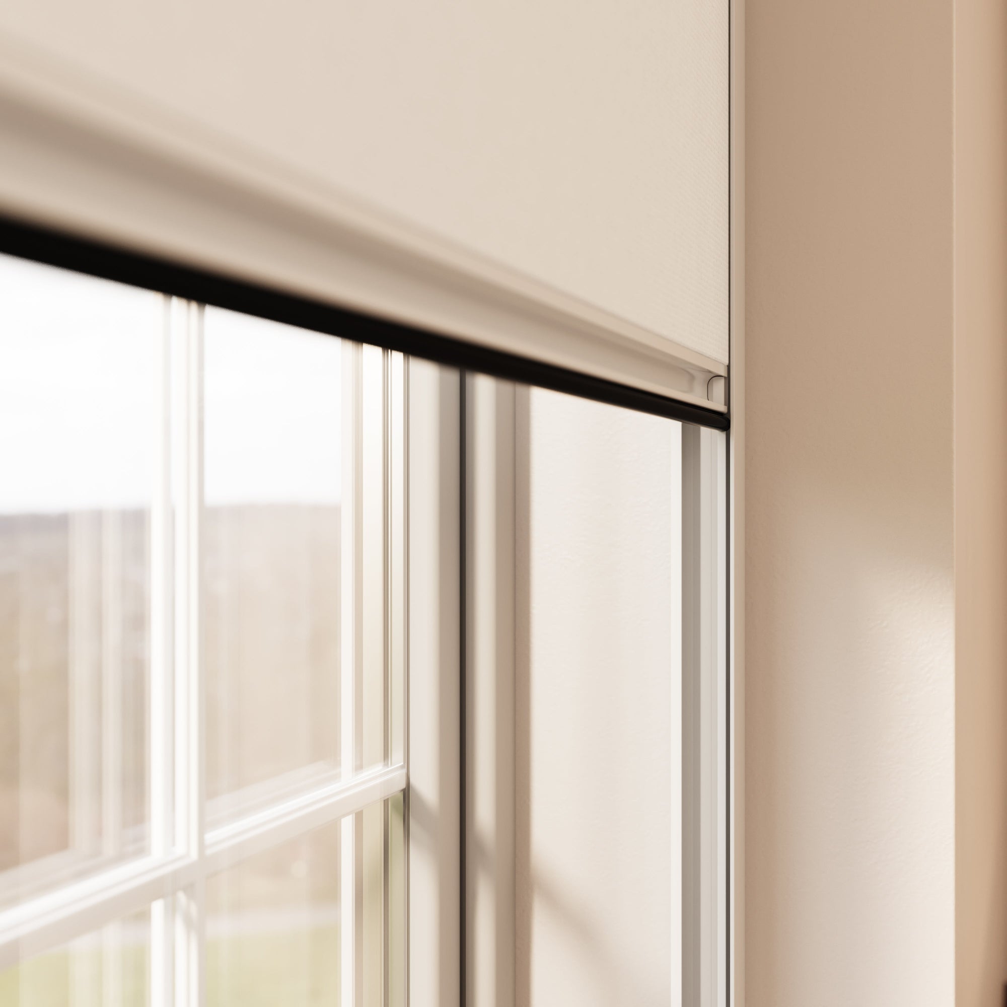 A close-up view of a window with white BlocOut blinds partially down. The window frame is white, and the wall next to the window is painted in a light beige colour. The scene outside the window shows a blurred outdoor landscape with natural light coming through.