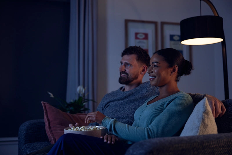 Couple sitting on the sofa eating popcorn in a dimly lit room.